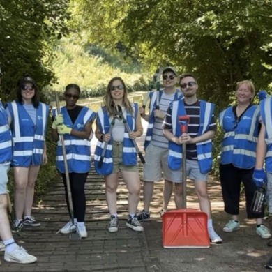 Members of the WPR team in blue high vis jackets, holding rakes and spades, in front of the canal during their canal clean up day