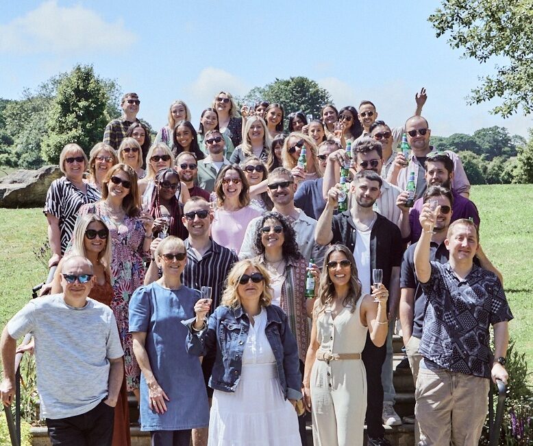 The WPR agency team standing on steps on a sunny day and raising glasses