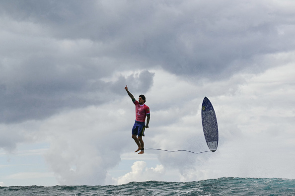 Gabriel Medina suspended above the waves next to his surfboard at the Olympics 2024