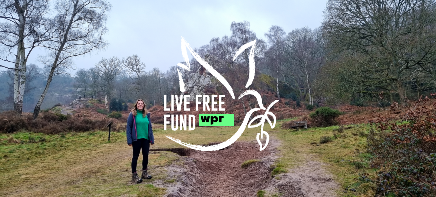 Emily standing in a valley with trees behind her and the Live Free Fund logo - an outline of a dove - beside her